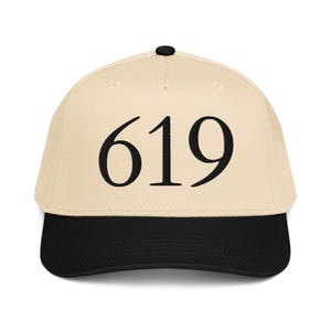 Puede incluir: Gorra de béisbol con corona color crema y visera negra. El número "619" se muestra en letras negras grandes y en negrita en la parte delantera. La gorra tiene un botón negro en la parte superior.