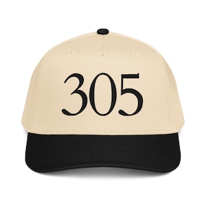 Puede incluir: Gorra de béisbol beige con visera negra y botón negro en la parte superior. El número "305" está bordado en negro en la parte delantera. Un accesorio clásico e informal.