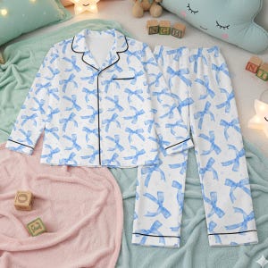 Può includere: Set pigiama bianco con motivo a fiocchi blu. La parte superiore a maniche lunghe e i pantaloni hanno finiture nere. Il pigiama è realizzato in un materiale morbido ed è progettato per il comfort. Adatto per dormire o rilassarsi.