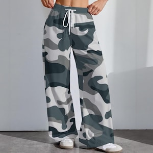 May include: Wide-leg pants with a camouflage pattern in shades of gray, white, and dark teal. The pants have a drawstring waist and are made of a lightweight fabric. The pants are shown with white sneakers.