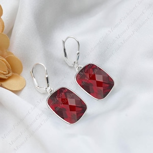 May include: A pair of silver earrings with red gemstone drop pendants. The gemstones are faceted and have a rectangular shape.
