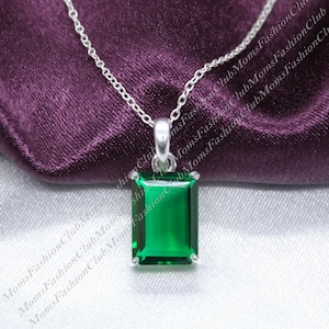 May include: A silver chain necklace with a pendant featuring a large, emerald green square-shaped gemstone.