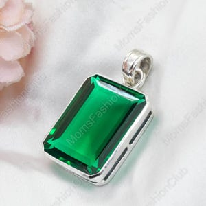 Pode incluir: Um pingente de prata com uma grande pedra rectangular de cor verde esmeralda. O pingente tem um design simples e elegante.