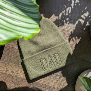 May include: A green knitted beanie with the word "DAD" embroidered in black on the front.