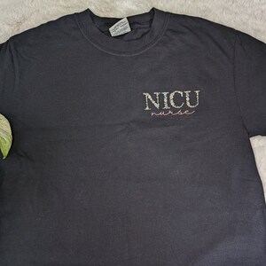 K&ouml;nnte beinhalten: Schwarzes T-Shirt mit dem Text "NICU nurse" in bunten Buchstaben.