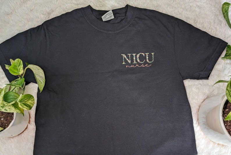 K&ouml;nnte beinhalten: Schwarzes T-Shirt mit dem Text "NICU nurse" in bunten Buchstaben.