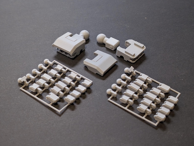 May include: A collection of light gray plastic model kit parts, including several rectangular components and small ball-shaped pieces. Two sprues with numerous small parts are also present, all arranged on a dark surface.