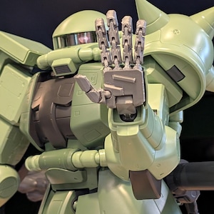 Op de afbeelding: Gedetailleerde afbeelding van een lichtgroene robot met gearticuleerde handen die een stopgebaar maken. De robot heeft een afgeronde kop, een hoekig lichaam en diverse mechanische details. De hand is zilver.