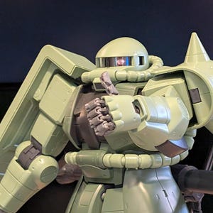Op de afbeelding: Een lichtgroen model van een robot met een afgeronde kop, een schild op de linkerschouder en een groot wapen aan de rechterkant. De robot heeft beweegbare gewrichten en een gedetailleerd ontwerp, tegen een donkere achtergrond.
