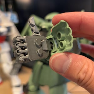 Op de afbeelding: Close-up van een grijze en groene modelbouwkit hand. De hand is gearticuleerd en lijkt deel uit te maken van een groter robotmodel. De hand wordt tegen een groen plastic stuk gehouden, mogelijk de arm.