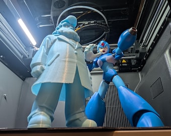 May include: Two action figures, one resembling a scientist in a light blue coat and hat, and another, a blue and white robot character, are positioned inside a 3D printer. The figures are detailed and appear to be recently printed.