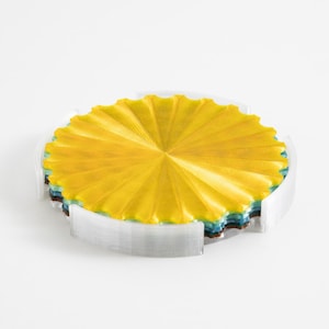 May include: A set of colorful coasters. The top coaster is a bright yellow with a radial design. The coasters are stacked in a clear holder, with visible layers of blue, green, and brown. The holder has a curved edge.