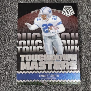 May include: A football trading card featuring Emmitt Smith of the Dallas Cowboys in a white and blue uniform. The card has the words "TOUCHDOWN MASTERS" and a football graphic in the background. The Mosaic logo is in the upper right corner.