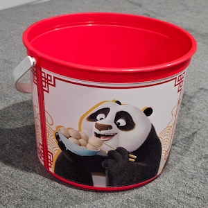 以下が含まれることがあります： 赤いプラスチック製のバケツ。パンダが餃子を持っているグラフィックが描かれています。バケツには白いハンドルと赤い縁があります。パンダは笑顔で、餃子が入った青いスプーンを持っています。