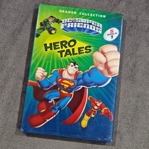 Puede incluir: Un libro de la colección de lectura "Hero Tales" de DC Super Friends. La portada presenta a Superman, Green Lantern y Flash. El libro es verde y azul con el texto "5 libros en 1".