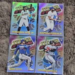 May include: Four baseball trading cards featuring players Fernando Tatis Jr., Vladimir Guerrero Jr., Juan Soto, and Samuel Basallo. Each card has a holographic background with the words "Titans of the Game".