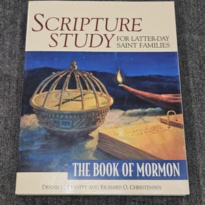 May include: A book titled "Scripture Study for Latter-day Saint Families" with "The Book of Mormon" on the cover. The cover art features a golden compass-like object, a lit lamp, and a night sky background.
