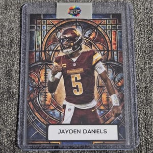 May include: A sports trading card featuring Jayden Daniels in a burgundy and gold Commanders uniform with the number 5. The background displays a stained-glass window pattern. A Custom Blast logo is at the top, and the name Jayden Daniels is printed at the bottom.