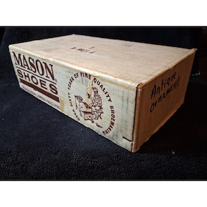 May include: A rectangular cardboard box with white and brown text. The side displays MASON SHOES, a graphic of a shoemaker, and the text OVER SIXTY YEARS OF FINE QUALITY SHOEMAKING. The end panel has the handwritten text Antique Ornament.