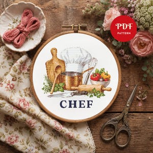 Peut inclure: Un projet de broderie au point de croix dans un tambour en bois représentant une toque de chef, une casserole en cuivre, une planche à découper, un rouleau à pâtisserie, un fouet, un couteau et des légumes avec le mot CHEF en lettres bleues.