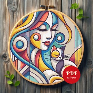 Puede incluir: Un colorido patrón de punto de cruz de una mujer y un gato, enmarcado en un aro de madera. El diseño presenta el rostro de una mujer con los ojos cerrados, cabello suelto y un gato. La paleta de colores incluye azul, amarillo, rojo y blanco. La imagen tiene una etiqueta "PDF PATTERN".