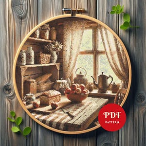 May include: A cross-stitch pattern of a rustic kitchen scene, framed in a wooden hoop. The design features a wooden table with a bowl of apples, a window with curtains, and shelves with jars and a teapot. The text "PDF PATTERN" is in a red circle.