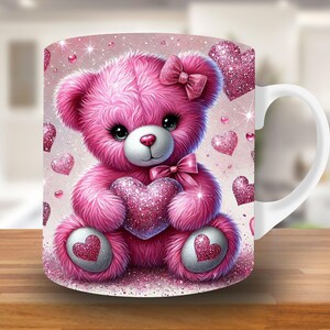 May include: A white ceramic mug with a pink teddy bear holding a pink heart. The mug is decorated with pink glitter hearts.
