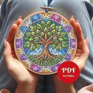 Peut inclure: Un motif de point de croix d'un arbre avec des feuilles vertes et un tronc brun, entouré d'une bordure florale colorée. Le motif est présenté dans un cercle à broder en bois. Le texte "PDF PATTERN" est dans un cercle rouge.