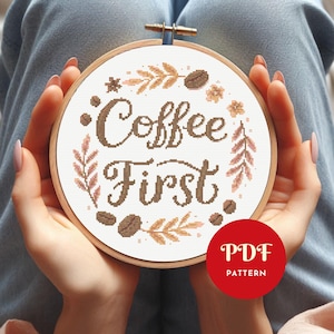 May include: A round embroidery hoop with the words "Coffee First" stitched in brown thread. The design includes coffee beans and floral accents in shades of brown and beige. A red circle with "PDF PATTERN" is in the lower right.