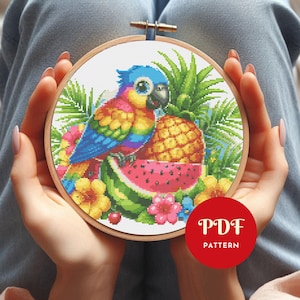 May include: A colorful cross-stitch embroidery hoop featuring a parrot, pineapple, and watermelon. The parrot has blue, yellow, and red feathers. The design includes tropical flowers and foliage. The text "PDF PATTERN" is in a red circle.