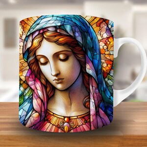 May include: A white ceramic mug with a stained glass design of a woman with a blue and purple robe. The woman's face is detailed with brown eyes and a soft smile.