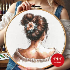 Op de afbeelding: Borduurpatroon van een vrouw met bruin haar in een knot, die een witte trui draagt. De vrouw kijkt weg van de kijker en heeft een bloem in haar haar. Het patroon is in een hoepel en de tekst "PDF PATTERN" is zichtbaar in de rechterbenedenhoek.