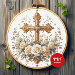 May include: A cross-stitch pattern featuring a detailed golden cross surrounded by white roses and floral accents. The design is set within a wooden embroidery hoop. A red circle with the text "PDF PATTERN" is visible.