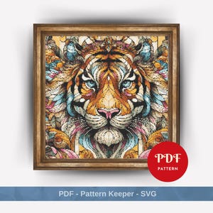 May include: A colourful, abstract cross-stitch pattern of a tiger's face. The tiger's fur is a mix of orange, yellow, blue, pink, and white. The pattern is framed in a brown wooden frame. The text "PDF PATTERN" is in a red circle in the bottom right corner.
