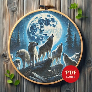 May include: A circular embroidery hoop containing a cross-stitch pattern of a pack of wolves howling at a large, bright full moon in a dark blue forest setting. A red circular badge with the white text PDF PATTERN is overlaid on the image.