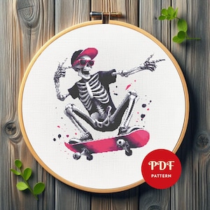 May include: Cross-stitch pattern featuring a skeleton skateboarding, wearing a black shirt, red sunglasses, and a red cap. The design includes a pink skateboard and is set in a wooden embroidery hoop. The words "PDF PATTERN" are in a red circle.