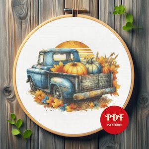 以下が含まれることがあります： 夕焼けを背景に、カボチャと秋の葉を運ぶヴィンテージの青いピックアップトラックのクロスステッチパターン。 デザインは木製の刺繍枠に収められています。 右下には「PDF PATTERN」と書かれた赤い円があります。