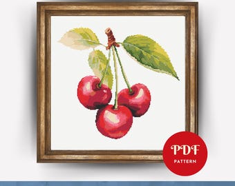 May include: A cross-stitch pattern featuring three bright red cherries with green leaves and brown stems, displayed in a wooden frame. A red circular badge in the bottom right corner contains the white text PDF PATTERN.