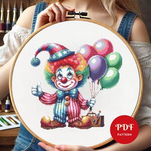 May include: Cross-stitch pattern of a colorful clown holding balloons and giving a thumbs-up. The clown wears a striped outfit, a rainbow wig, and a hat with stars. A brown suitcase sits at the clown's feet. The text "PDF PATTERN" is in a red circle.
