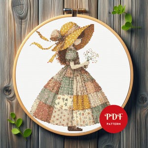 May include: Cross-stitch design of a girl in a patchwork dress and a large yellow hat, holding flowers. The design is framed in a wooden embroidery hoop. A red circle with "PDF PATTERN" is in the lower right corner.