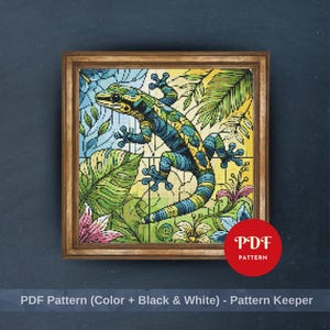 May include: Cross-stitch pattern of a gecko in a tropical setting, framed in a wooden frame. The gecko is blue and yellow, surrounded by green leaves and pink flowers. The text "PDF Pattern" is in a red circle.