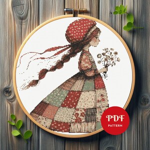 May include: Cross-stitch pattern of a girl in a patchwork dress, holding flowers, within a wooden embroidery hoop. The girl wears a red polka-dot bonnet and has a long braid. The PDF pattern is indicated by a red circle.