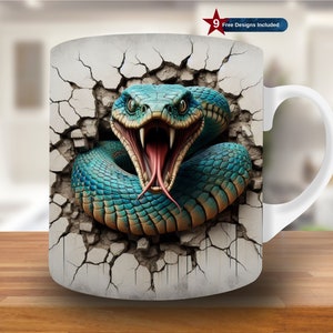 Puede incluir: Taza de cerámica blanca con un gráfico de una serpiente verde y azul rompiendo una pared agrietada. La serpiente tiene la boca abierta con colmillos afilados y una lengua roja.