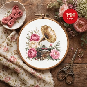May include: A cross-stitch embroidery project in a wooden hoop featuring a vintage gramophone surrounded by pink and cream-colored peonies. The design is printed on white fabric. A red circular badge with the white text PDF PATTERN is visible.