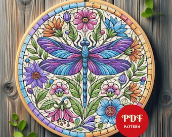 May include: A cross-stitch pattern featuring a dragonfly with purple and blue wings, surrounded by colorful flowers and green leaves. The design is set in a wooden embroidery hoop. The text "PDF PATTERN" is in a red circle.