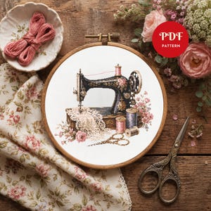 May include: A cross-stitch pattern in a wooden embroidery hoop featuring a black vintage sewing machine, lace fabric, spools of thread, and pink floral accents. A red circular graphic with the white text PDF PATTERN is visible in the corner.
