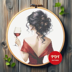 May include: Cross-stitch pattern of a woman in a red dress holding a glass of red wine, viewed from the back. The design is set in a wooden embroidery hoop. The text "PDF PATTERN" is in a red circle.