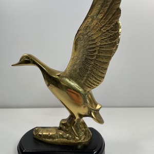 Vintage Brass duck taking a flight on a wooden stand