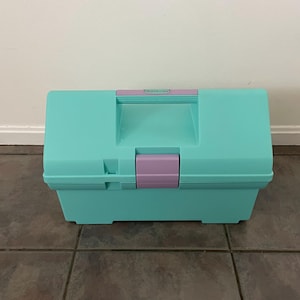 May include: A turquoise plastic storage box with a purple handle and latch. The box has the word "Rubbermaid" printed on the top.