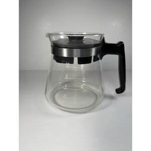 May include: A clear glass coffee carafe featuring a black plastic lid and a matching black handle. The glass body includes white measurement markings for 4, 6, 8, and 10 units, with a silver-toned metal band encircling the top section below the lid.